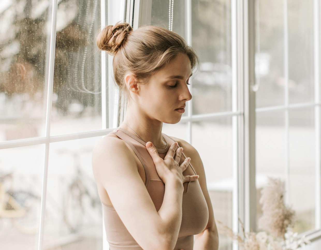 woman meditating in well lit room with hand on her chest